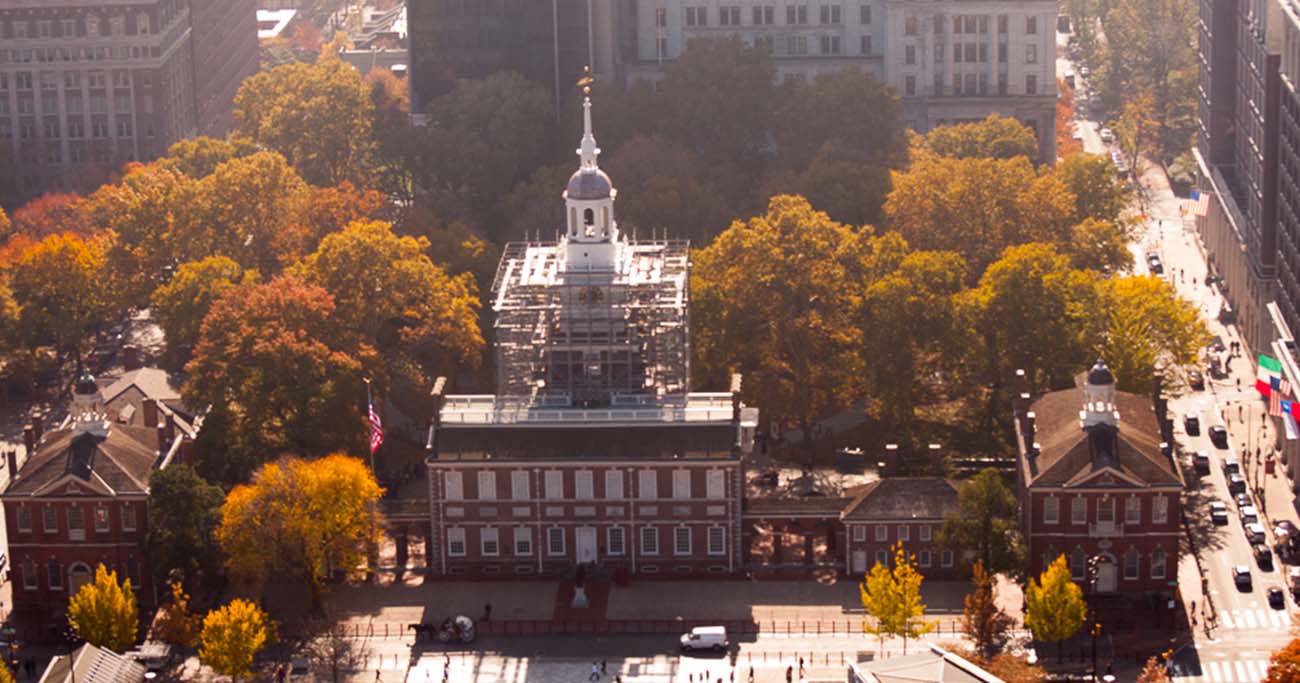 Aerial view of Independence Hall surrounded by autumn foliage and urban streets.