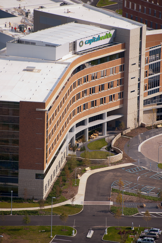 Aerial view of a modern hospital building with curved brick architecture and surrounding parking and landscaping.